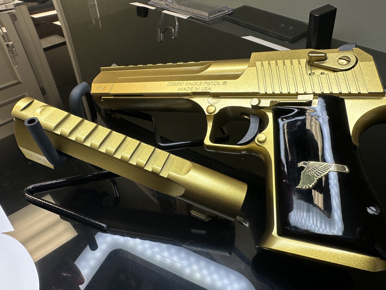 Desert Eagle .50AE handgun in gold Cerakote with eagle emblem grip on shop display case